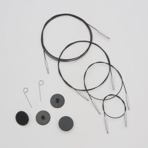 May include: A collection of black circular knitting needles with silver tips, black circular stoppers and silver stitch holders, arranged on a white surface. The needles are of varying sizes.