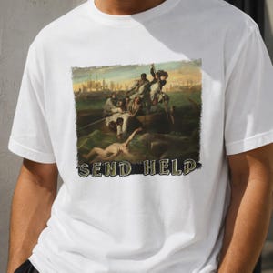 May include: A white short-sleeve t-shirt featuring a graphic print of a classical painting depicting a group of people in a boat on turbulent water. Below the artwork, the text "SEND HELP" is printed in a bold, dark, serif font style.