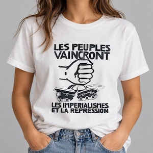 May include: A white short-sleeve t-shirt featuring a black graphic print of a fist crushing a tank. The text above the fist reads "LES PEUPLES VAINCRONT" and the text below the tank reads "LES IMPERIALISMES ET LA REPRESSION" in bold black letters.