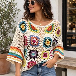 Könnte beinhalten: Ein cremefarbenes Häkeloberteil mit einem Muster aus bunten Granny Squares in Gelb, Rot, Blau, Grün und Violett. Das Kleidungsstück hat weite Ärmel mit horizontalen Regenbogenstreifen und ein offenes, kompliziertes, spitzenartiges Strickmuster.