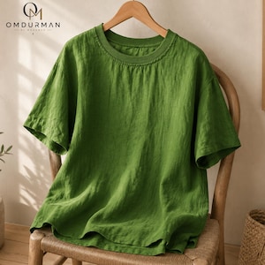 May include: A solid grass green short-sleeved t-shirt with a ribbed crew neckline. The garment features a relaxed fit and a textured fabric surface. The OMDURMAN BY MOHAMED logo is visible in the upper left corner of the image.