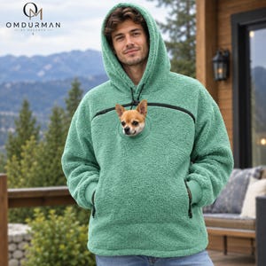 Könnte beinhalten: Ein mintgrüner Kapuzenpullover aus Sherpa-Fleece mit großer Kapuze, langen Ärmeln mit gerippten Bündchen und einer zentralen Kängurutasche. Ein kleiner beigefarbener und weißer Chihuahua schaut aus einer runden Öffnung im Brustbereich heraus.