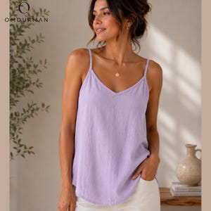 May include: A light purple sleeveless camisole top featuring a V-neckline and thin spaghetti straps. The garment is made of a textured fabric and has a relaxed fit. The top is plain with no patterns or prints, showcasing a simple design.