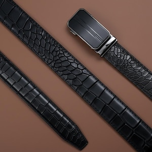 Op de afbeelding: Een zwarte riem met een gestructureerd krokodillenpatroon en een rechthoekige automatische schuifgesp. De gesp is matzwart met een metallic zilverkleurige rand en een subtiel verticaal lijndesign op de voorzijde van de sluiting.