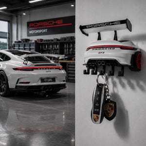 May include: A white wall-mounted key holder shaped like the rear of a Porsche GT3, featuring a black spoiler with the Porsche logo, red taillights, and five black hooks. A silver and black car key fob with a Porsche crest keychain hangs from one hook.