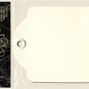 May include: A white tag with a scalloped edge and a silver metal ring. The tag is blank and ready to be used for gift wrapping or other crafting projects.