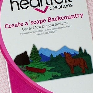 May include: A pink and white package of 6 heart felt creations craft dies. The package features a scenic image of a wolf, mountains, trees, and a canoe. The text on the package reads "Create a 'scape Backcountry" and "Use In Most Die-Cut Systems".