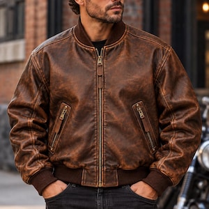 May include: A brown distressed leather bomber jacket featuring a ribbed collar, cuffs, and hem, a central metal zipper closure, and two slanted front pockets with zipper detailing. The jacket has a worn-in texture and a dark brown finish.