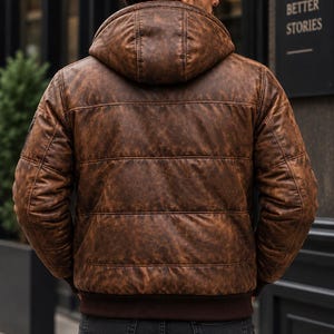 May include: A brown distressed leather puffer jacket with a hood and dark brown ribbed cuffs and hem. The jacket features horizontal quilted stitching across the back and sleeves, providing a textured appearance with varied brown tones.