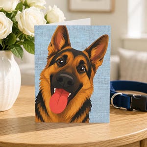 May include: A greeting card featuring a vibrant illustration of a German Shepherd dog with pointed ears, a black muzzle, and a bright red tongue hanging out, set against a light blue textured background that mimics a woven fabric pattern.