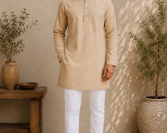Può includere: Una kurta beige a maniche lunghe con colletto alla coreana e abbottonatura parziale, abbinata a pantaloni bianchi semplici e sandali in pelle marrone scuro. Il capo presenta un design pulito in tinta unita con maniche lunghe e orlo dritto.