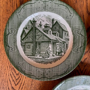 Puede incluir: Un plato de cena de cerámica verde y blanco con una ilustración en blanco y negro de un edificio histórico con personas caminando frente a él. El plato tiene un borde verde con un diseño decorativo.