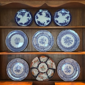 May include: A wooden cabinet displays a collection of antique plates. The plates feature blue and white floral patterns, with varying designs and sizes. The cabinet is made of dark wood, and the plates are arranged on shelves.