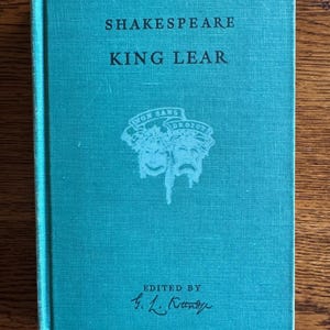 May include: A teal-colored hardcover book titled "SHAKESPEARE KING LEAR" with white text. The cover features a white emblem with two theatrical masks and the text "HONI SOIT QUI MAL Y PENSE". The book is edited by G. L. Kittredge.