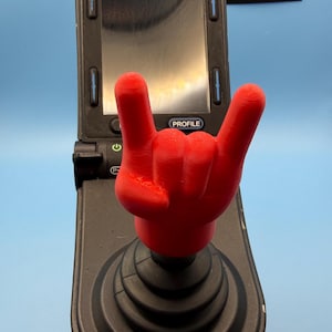 Op de afbeelding: Een felrode 3D-geprinte joystick-opzetstuk in de vorm van een rock-and-roll handgebaar, bevestigd op een zwarte joystick-controller. De controller heeft een digitaal scherm met de tekst PROFILE en een aan-uitknop icoon. Het logo FCLight DESIGNS is zichtbaar.