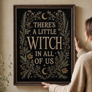 Könnte beinhalten: Ein rechteckiges gerahmtes Wandbild mit schwarzem Hintergrund und goldfarbenem Text im Stickerei-Stil, der THERE'S A LITTLE WITCH IN ALL OF US lautet. Das Design ist von einer botanischen Bordüre aus goldenen und grünen Blättern, Blumen und Monden umgeben.