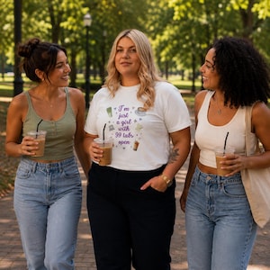 May include: A white t-shirt featuring the purple text "I'm just a girl with 99 tabs open" alongside small illustrations of drinks and computer icons. The shirt is worn with black trousers, while the other two individuals wear tank tops and jeans.