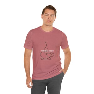 Könnte beinhalten: Ein altrosa T-Shirt mit kurzen Ärmeln und einer schwarzen Strichgrafik einer Kaffeetasse mit aufsteigendem Dampf. Der Text "I TURN COFFEE INTO CODE" ist in weißen Großbuchstaben mittig über der Kaffeetassengrafik aufgedruckt.
