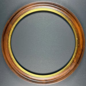 May include: A circular picture frame featuring a wide, polished dark brown wooden outer border and a thin, smooth gold-toned inner rim. The frame has a rounded profile and a consistent, symmetrical design, presenting a classic look for displaying artwork.