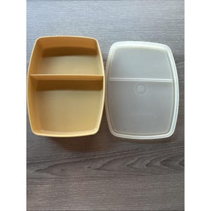 May include: A rectangular mustard yellow plastic food storage container with a single interior divider and a matching translucent white plastic lid. The container and lid both feature rounded corners and a smooth, matte finish throughout.