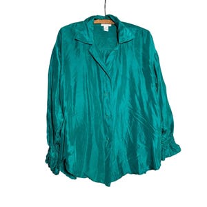 May include: A long-sleeved button-down shirt in a vibrant emerald green color. The shirt features a classic collar, a front button placket, and gathered cuffs at the wrists. The fabric has a subtle sheen and a fluid, relaxed drape throughout.