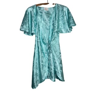 May include: A light turquoise satin robe featuring a tonal floral jacquard pattern, short flutter sleeves, and a front tie closure. The garment has a V-neckline and a label at the inner collar. The fabric has a shiny finish and a smooth texture.