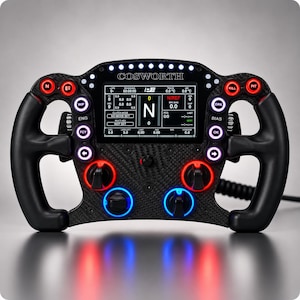 Op de afbeelding: Een zwart racestuur van koolstofvezel met een centraal digitaal display met de tekst COSWORTH. Het apparaat bevat meerdere verlichte knoppen, draaiknoppen met rode en blauwe lichtringen en een rij led-lampjes aan de bovenzijde.