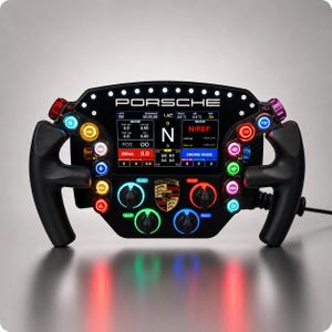 Può includere: Un volante da corsa Porsche nero dotato di uno schermo digitale centrale con vari dati di telemetria, pulsanti multicolori illuminati, manopole rotanti e il logo Porsche. Il dispositivo presenta etichette come PORSCHE, N, N/REF e varie abbreviazioni tecniche.