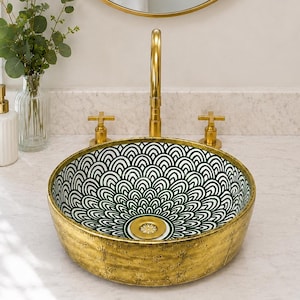 May include: A round vessel sink with a textured gold exterior and a white interior featuring a dark green fan-shaped pattern. The sink includes a gold drain and is paired with a gold faucet and two gold cross-handle knobs on a white countertop.