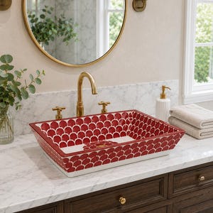 May include: A rectangular vessel sink featuring a repeating red and white scalloped pattern on the interior and exterior surfaces. The sink is equipped with a gold-toned tap and two matching cross-handle knobs, set against a white marble countertop.