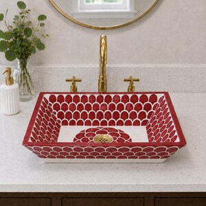 May include: A rectangular ceramic vessel sink featuring a hand-painted red and white scalloped pattern on the interior and exterior walls, with a central floral motif at the base and a gold-toned metal drain fixture centred in the basin.