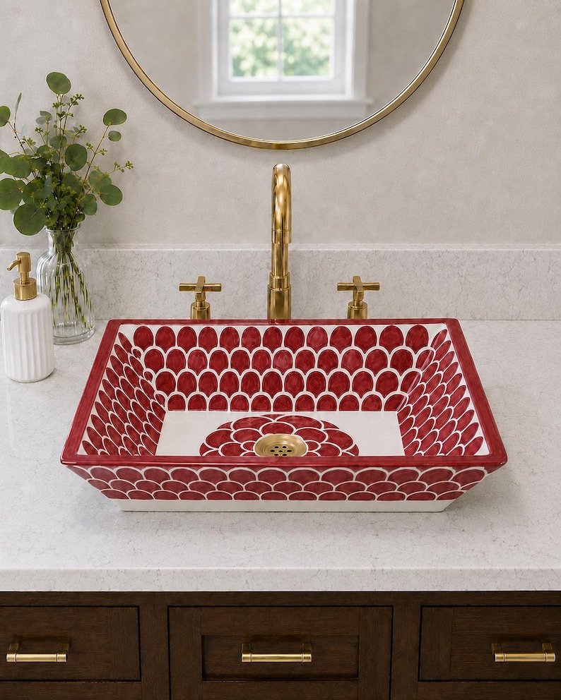 May include: A rectangular ceramic vessel sink featuring a hand-painted red and white scalloped pattern on the interior and exterior walls, with a central floral motif at the base and a gold-toned metal drain fixture centred in the basin.
