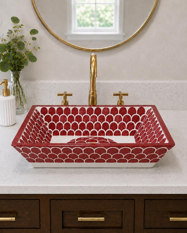 May include: A rectangular ceramic vessel sink featuring a repeating red and white scalloped pattern across its interior and exterior surfaces. The sink is paired with a tall, brushed gold faucet and two matching cross-handle knobs on a white countertop.