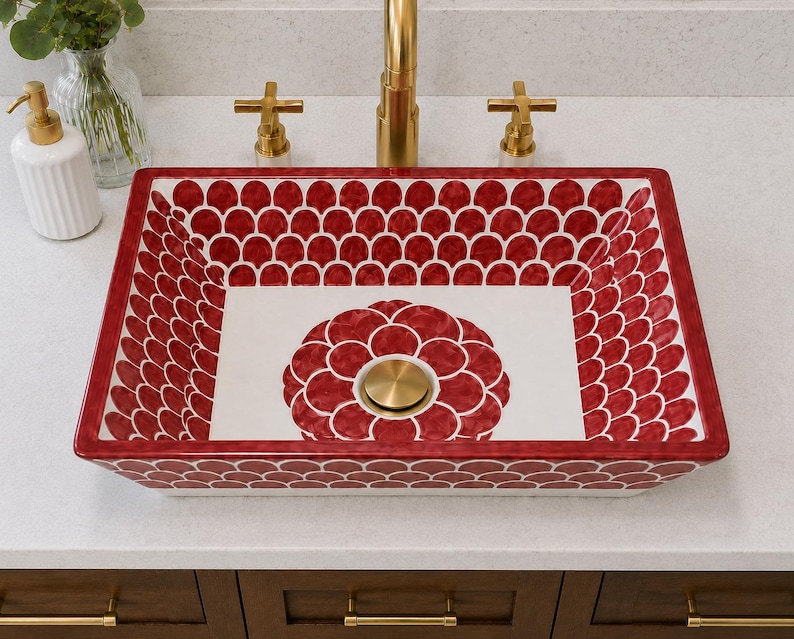 May include: A rectangular ceramic vessel sink featuring a white base with a repeating red scalloped pattern along the interior walls and a large red floral motif at the centre. The sink includes a circular brass drain plug centred in the basin.