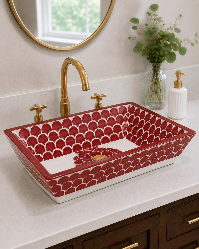 May include: A rectangular ceramic vessel sink featuring a repeating red and white scalloped pattern on the interior and exterior walls. The basin includes a central circular floral motif surrounding the drain and a gold-toned metal faucet fixture.