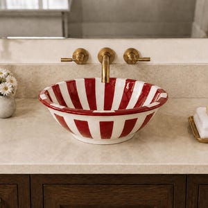 Peut inclure: Une vasque ronde en céramique ornée d'un motif à rayures verticales rouges et blanches. Le lavabo est installé sur un comptoir de couleur claire avec un robinet en laiton et deux poignées en laiton assorties fixées au mur au-dessus.