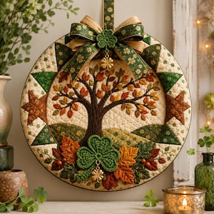May include: A circular quilted wall hanging featuring a central tree with autumn-coloured leaves. The border displays green and cream star patterns. A large green fabric bow with gold shamrocks sits at the top, accented by a gold metal clover charm.