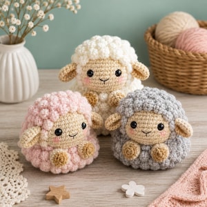 Pode incluir: Três pequenos brinquedos de ovelha feitos de crochê, redondos, nas cores branca, rosa claro e cinza claro. Cada ovelha apresenta um corpo de lã encaracolada texturizada, um rosto bege liso com olhos de botão pretos e bochechas rosadas.