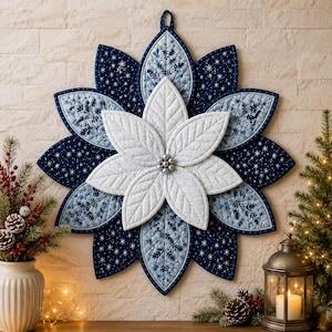 Könnte beinhalten: Ein gesteppter Wandbehang aus Stoff in Form einer mehrschichtigen Blume mit spitzen Blütenblättern. Die Mitte besteht aus weißen Blütenblättern, umgeben von Schichten aus dunkelblauem Stoff mit Sternenmustern und hellblauem Stoff mit Blattdrucken.