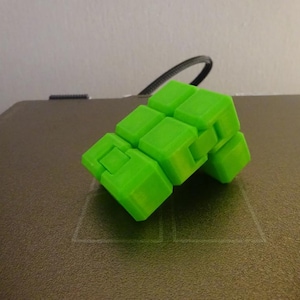 May include: A bright lime green infinity cube fidget toy composed of eight interconnected smaller cubes. The plastic structure features a smooth, matte finish and is articulated with hinges that allow the individual segments to fold and rotate.