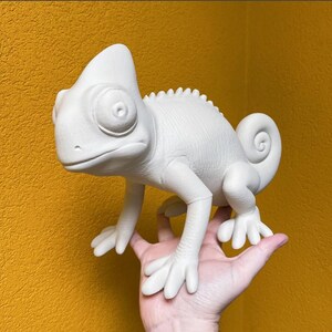May include: A matte white chameleon figurine featuring a textured surface, a prominent crest on its head, large circular eyes, and a curled tail. The reptile is depicted in a standing position with detailed toes and a smooth, uniform finish.