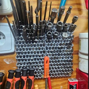 Könnte beinhalten: Ein hellgrauer Werkzeug-Organizer mit Wabenmuster, der eine Vielzahl von Metall-Schraubendreher-Bits, Inbusschlüsseln und Steckschlüssel-Adaptern enthält. Die Gitterstruktur hält zahlreiche kleine Handwerkzeuge aufrecht.