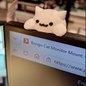 May include: A white 3D-printed Bongo Cat figure with black eyes and a black mouth, designed to sit on the top edge of a computer monitor. The screen displays the text Bongo Cat Monitor Mount and a partial URL starting with https://www.p.