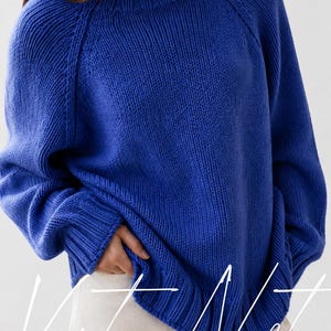 Può includere: Un maglione a maniche lunghe in un vibrante blu reale con girocollo a coste, maniche raglan, polsini e orlo a coste. Il capo è indossato sopra pantaloni chiari. Il testo Vanya Nest è sovrapposto in corsivo bianco nella parte inferiore.