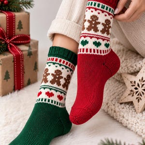 Puede incluir: Un par de calcetines de punto con un patrón festivo. Un calcetín es principalmente verde oscuro con una banda blanca que muestra hombres de jengibre marrones y corazones rojos. El otro es rojo con una banda blanca con hombres de jengibre y corazones verdes.