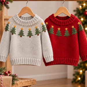 May include: Two long-sleeved knit jumpers hanging on wooden hangers. One jumper is light grey and the other is deep red. Both feature a repeating pattern of green pine trees with yellow stars at the top around the neckline and shoulders.