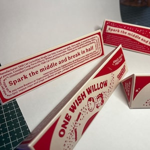 May include: Three triangular paper boxes with red and cream coloring. The text reads "ONE WISH WILLOW" and "Spark the middle and break in half." Graphics include small stars and two cartoon faces. The boxes contain instructions and warnings.
