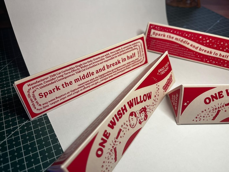 May include: Three triangular paper boxes with red and cream coloring. The text reads "ONE WISH WILLOW" and "Spark the middle and break in half." Graphics include small stars and two cartoon faces. The boxes contain instructions and warnings.
