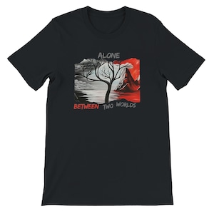 Könnte beinhalten: Ein schwarzes Kurzarm-T-Shirt mit einer zentralen Grafik eines kahlen Baumes zwischen einer graustufigen Landschaft und einer leuchtend roten Vulkanszene. Der Text ALONE steht über dem Baum und BETWEEN TWO WORLDS steht darunter.