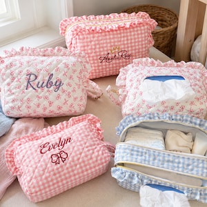 Può includere: Una collezione di pochette e custodie in tessuto trapuntato con bordi arricciati. Gli articoli sono decorati con motivi a quadretti rosa o fiocchi rosa, alcuni ricamati con nomi come Ruby, Amelia Rose ed Evelyn, altri progettati come porta fazzoletti.